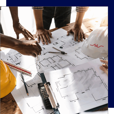 Close-up of a planning team reviewing building blueprints with hard hats and drafting tools, symbolizing early warehouse design and site evaluation. One of the hats bears the North American Steel Logo.