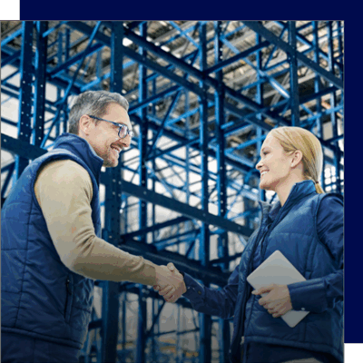 Two professionals shaking hands in front of an industrial racking system, representing successful collaboration on warehouse planning.