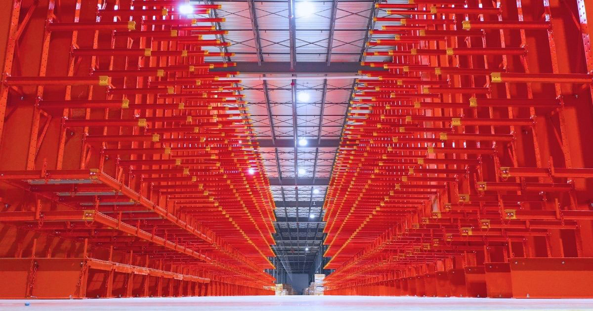 A symmetrical shot looking down a long aisle of heavy-duty orange cantilever racking designed for storing long or oversized loads.