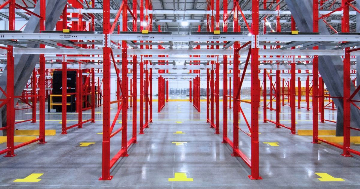 A wide-angle shot of a pushback racking system featuring bright red vertical uprights and gray nested carts on inclined rails.