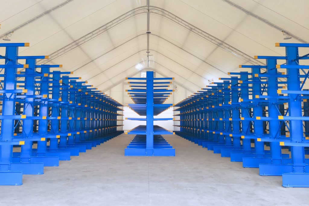 Symmetrical center-aisle perspective of heavy-duty blue cantilever racking runs configured inside an industrial shelter building.