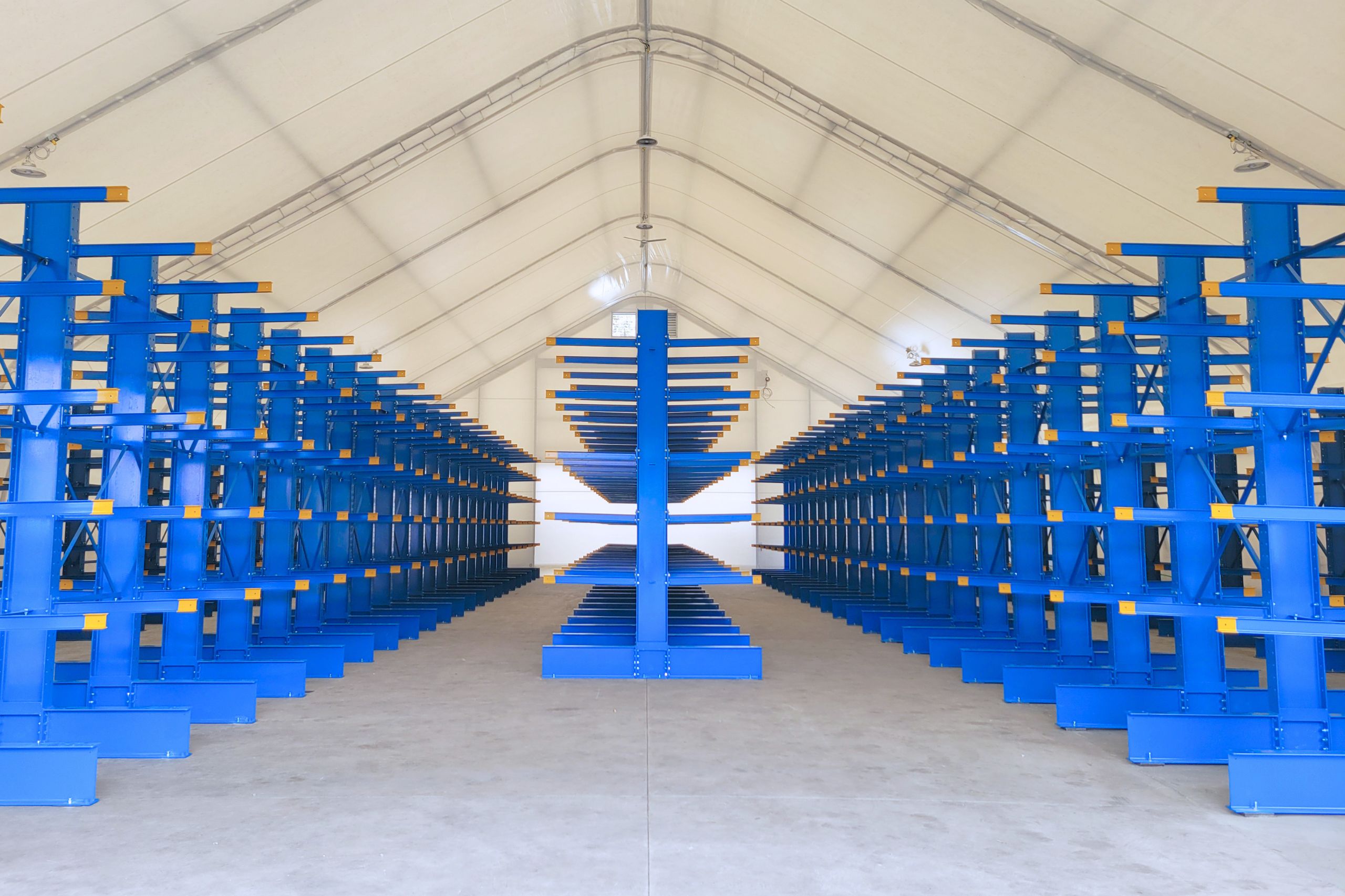 Symmetrical center-aisle perspective of heavy-duty blue cantilever racking runs configured inside an industrial shelter building.